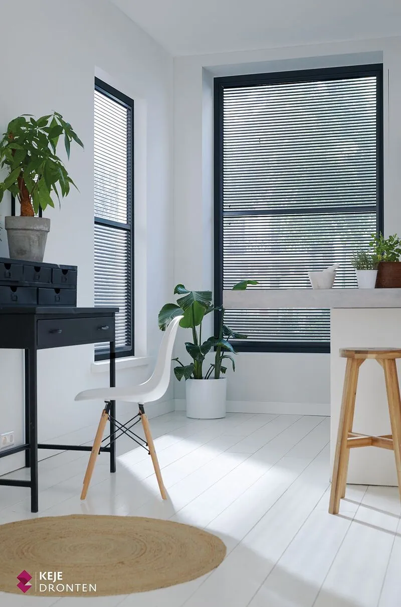Antraciet jaloezieën in frame in een moderne lichte werkruimte met witte vloer en kamerplanten