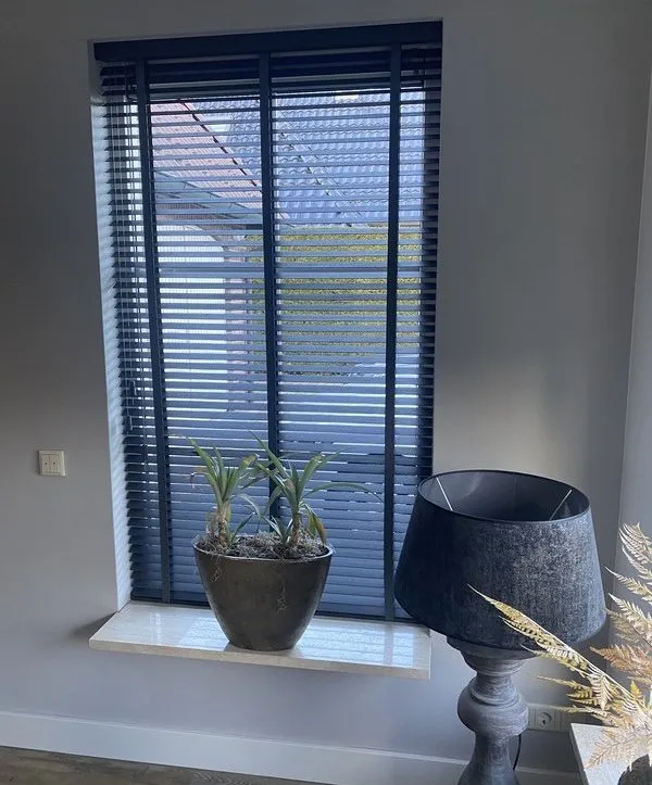 Houten jaloezie in antraciet in woonkamerraam met plant op vensterbank